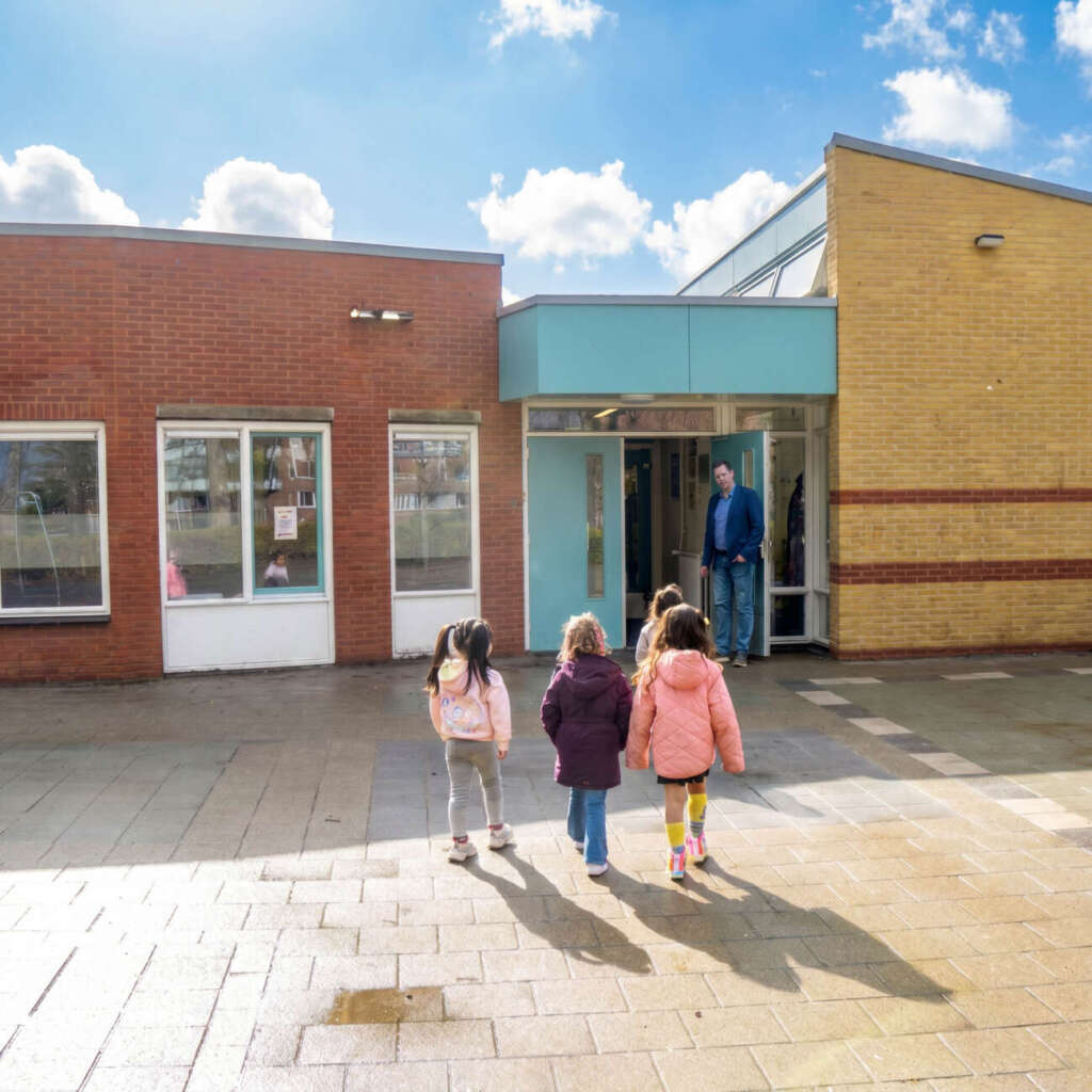 kinderen lopen naar binnen en worden verwelkomd door de directeur Jordy